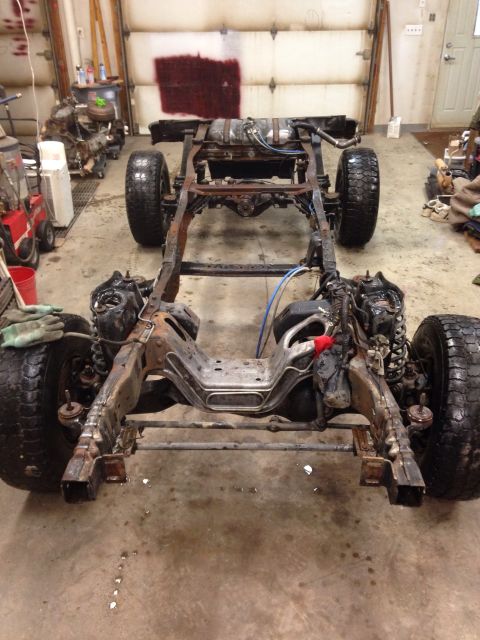 1993 Ford Bronco - The chassis of a vehicle is shown in a garage, with the body removed and parts disassembled.