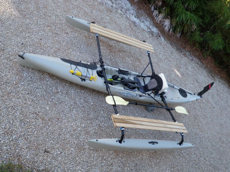 Kayak with wooden outriggers and seats attached, sitting on a gravel surface