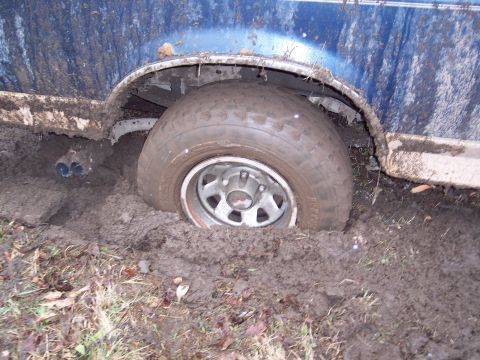 1987 Ford Bronco - A vehicle is stuck in thick mud, with its rear tire deeply embedded.