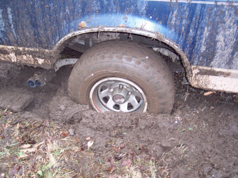 blue vehicle's rear tire sunk deep in mud, exhaust pipes visible