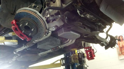 2003 Ford Crown Victoria - Underside view of a vehicle on a shop lift showing a drilled-and-slotted rotor, red brake caliper, and transmission pan.