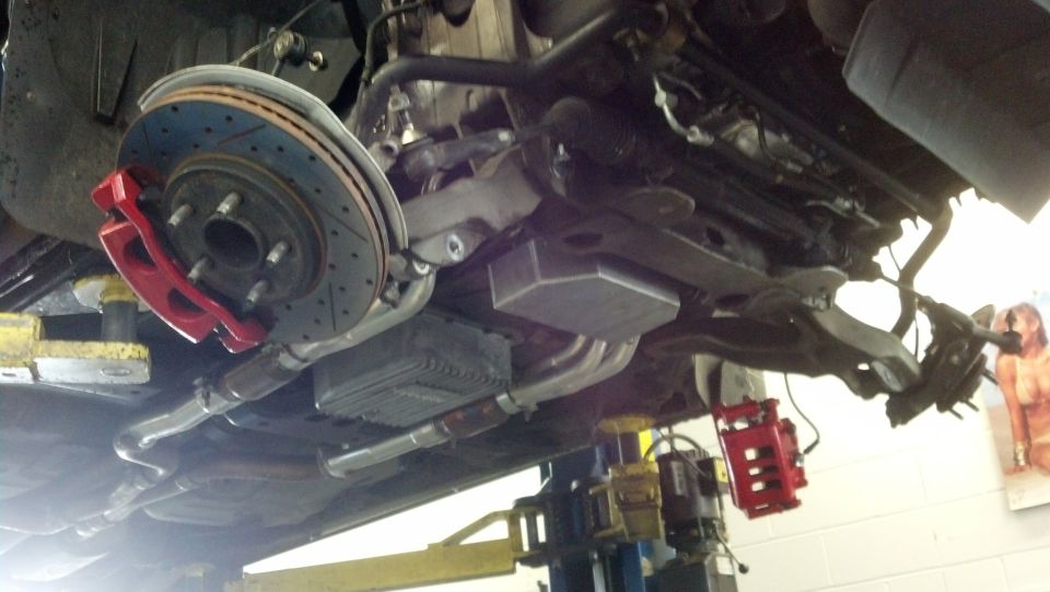 Undercarriage of a vehicle on a lift showing drilled rotor and red brake caliper