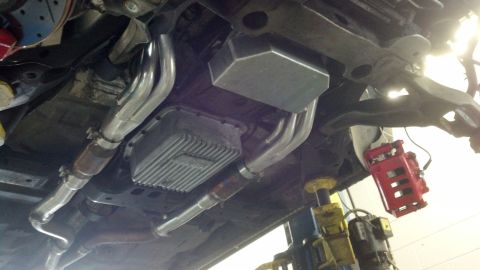 2003 Ford Crown Victoria - Undercarriage of a vehicle on a lift showing a finned transmission pan, dual exhaust piping, and a red brake caliper.