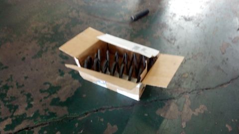 2003 Ford Crown Victoria - open cardboard box holding rows of dark drill bits resting on a worn, cracked green concrete shop floor.