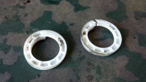 2003 Ford Crown Victoria - Two dirty white plastic coil-spring isolators or bearing rings lying on a worn green concrete floor.
