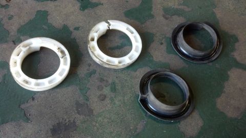 2003 Ford Crown Victoria - Two white plastic bearing rings and two black rubber isolator seats laid out on a worn green concrete floor.