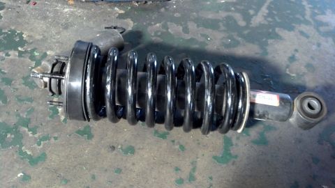 2003 Ford Crown Victoria - assembled strut and black coil spring with upper mount lying on a worn green concrete floor.