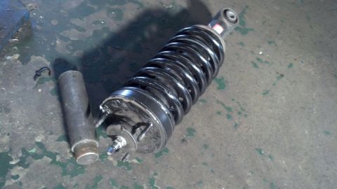 2003 Ford Crown Victoria - strut with black coil spring beside a heavy metal sleeve or spacer on a worn green concrete floor.