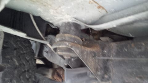 1992 Ford Bronco - Close-up view of the rusty undercarriage and suspension of a vehicle, with a tire visible on the left.