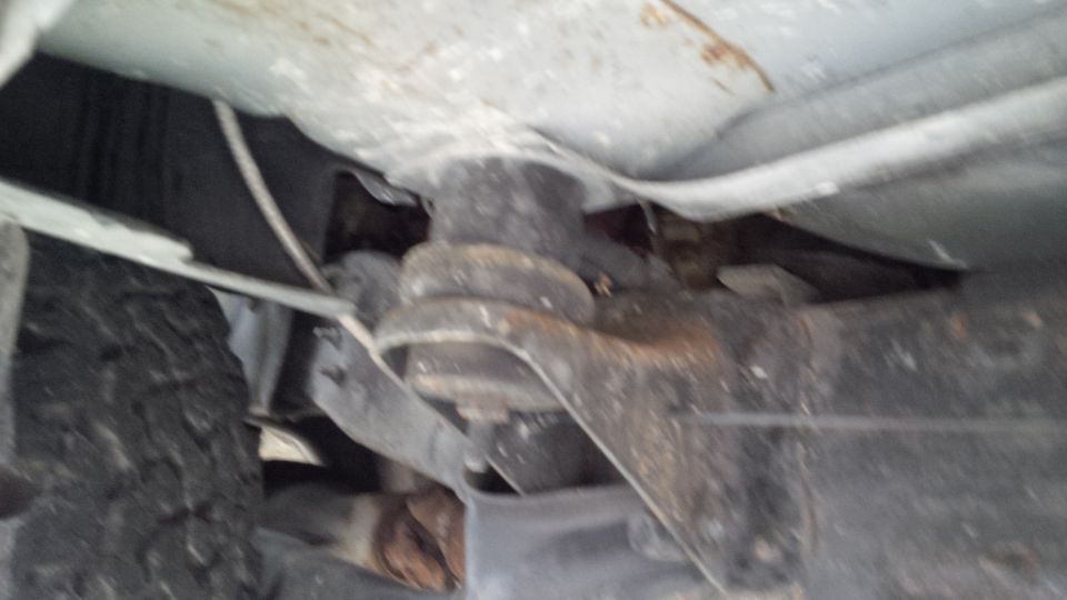 Undercarriage of a vehicle showing suspension components and a tire. The metal parts are rusty
