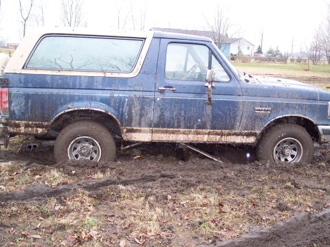 1987 Ford Bronco - This 1987 Ford Bronco is deeply stuck in thick mud, with its wheels submerged and the chassis resting on the ground.