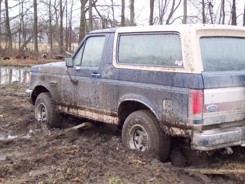 1987 Ford Bronco - This 1987 Ford Bronco is deeply stuck in thick mud, with trees and water in the background.