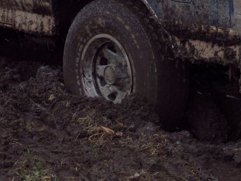 1987 Ford Bronco - This vehicle is deeply stuck in thick mud, with only the wheel and lower body visible.