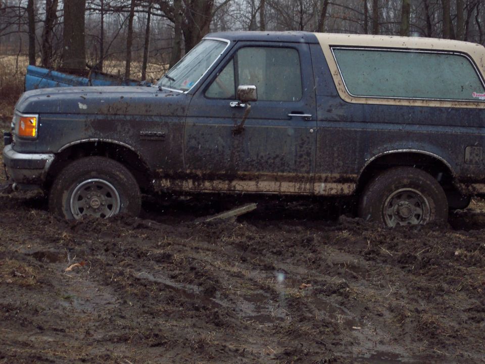 Mud-covered 1987 Ford Bronco, side view, stuck in deep mud with front wheels submerged