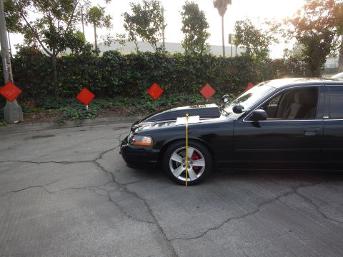 2003 Ford Crown Victoria - black full-size sedan sits lowered in a lot as a measuring tape gauges fender-to-ground ride height.