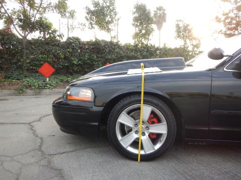 2003 Ford Crown Victoria - Yellow tape measure runs from the front fender to the ground over the alloy wheel of a black sedan.