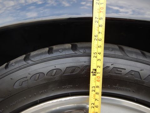 2003 Ford Crown Victoria - yellow tape measure spans a Goodyear tire sidewall and silver wheel under a partly cloudy sky.