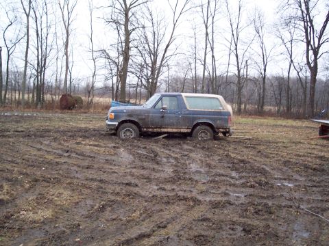 1987 Ford Bronco - This 1987 Ford Bronco is deeply stuck in a muddy field, with only its wheels and lower body visible above the mire.