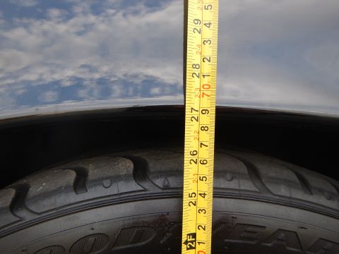 2003 Ford Crown Victoria - yellow tape measure is held vertically against a tire tread and dark vehicle fender lip.