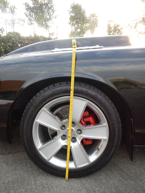 2003 Ford Crown Victoria - yellow tape measure runs from a black sedan's fender down past the alloy wheel and red brake caliper.