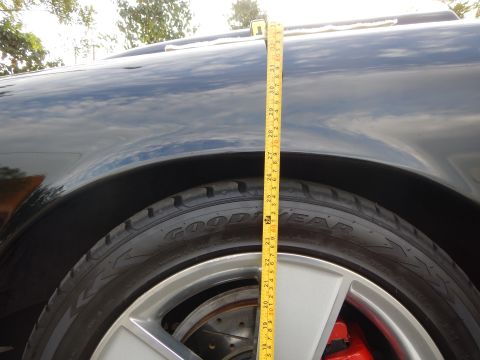 2003 Ford Crown Victoria - yellow tape measure gauges the fender-to-tire gap over a silver wheel on a dark sedan.