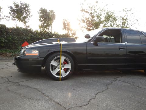 2003 Ford Crown Victoria - lowered black sedan photographed from the front three-quarter with a tape measure set at the front wheel.