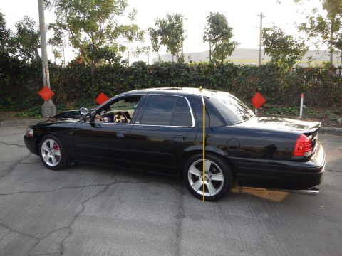 2003 Ford Crown Victoria - lowered black four-door sedan shown from the rear three-quarter with a tape measure at the rear wheel.