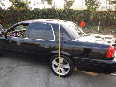 2003 Ford Crown Victoria - black sedan viewed from the side with a yellow tape measure stretched from the roof line to the ground.
