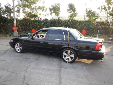 2003 Ford Crown Victoria - glossy black lowered sedan shown from the rear three-quarter in a lot with a tape measure at the rear wheel.