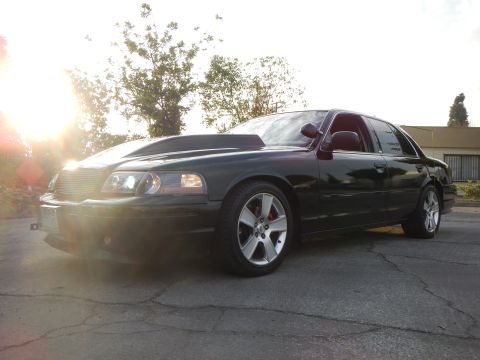 2003 Ford Crown Victoria - black full-size sedan with a billet grille is shot front three-quarter, backlit by a low setting sun.