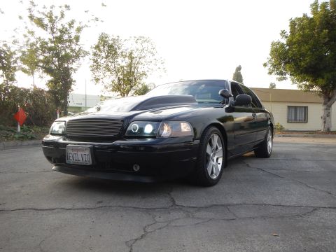 2003 Ford Crown Victoria - black full-size sedan with a billet grille and front plate reading EVIL VIC sits in a paved lot.