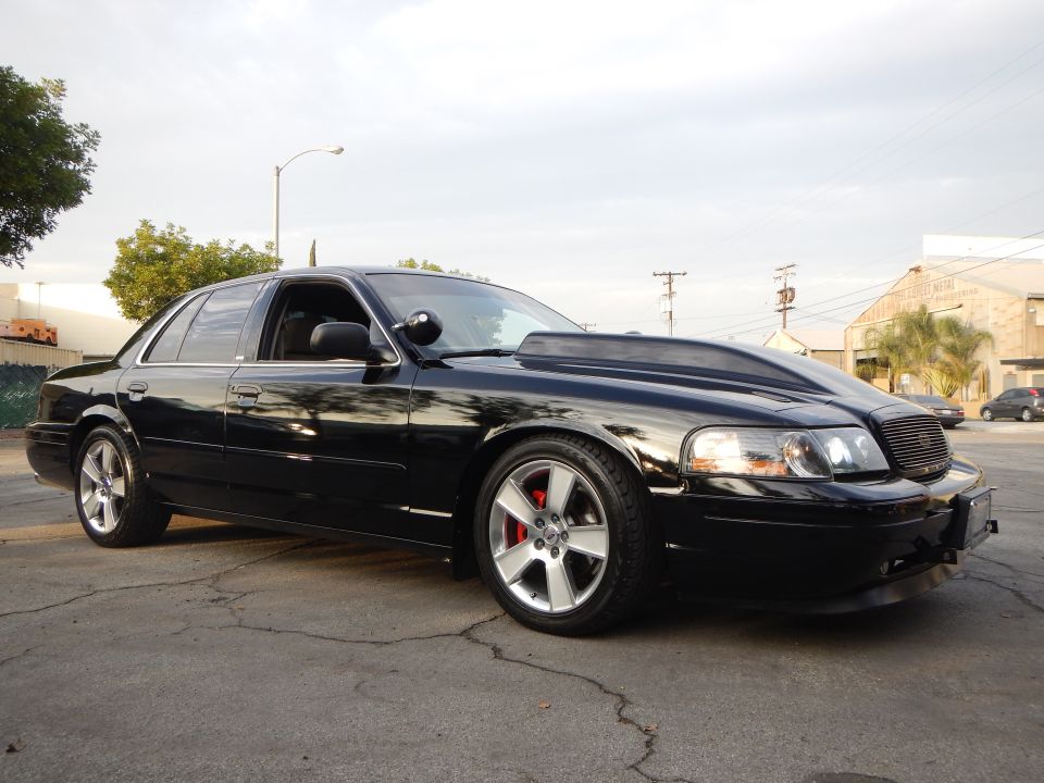Front three-quarter of a lowered black sedan with mesh grille and silver wheels