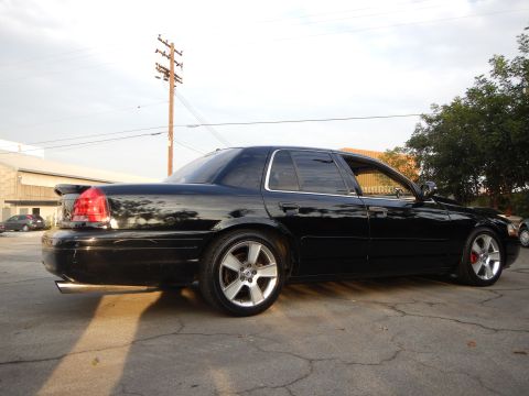 2003 Ford Crown Victoria - lowered black four-door sedan with silver alloy wheels shown from the rear three-quarter in a paved lot.