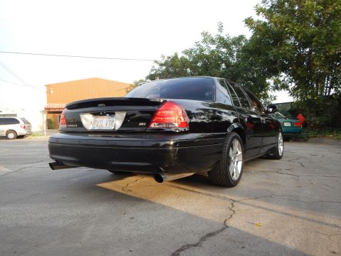 2003 Ford Crown Victoria - Rear three-quarter of a black sedan showing an EVIL VIC plate, an SVT-style badge and a dual exhaust tip.