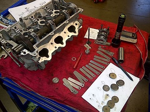 1995 Ford Probe - Disassembled engine cylinder head with various engine parts laid out on a red cloth, including valves, camshaft, and shims.