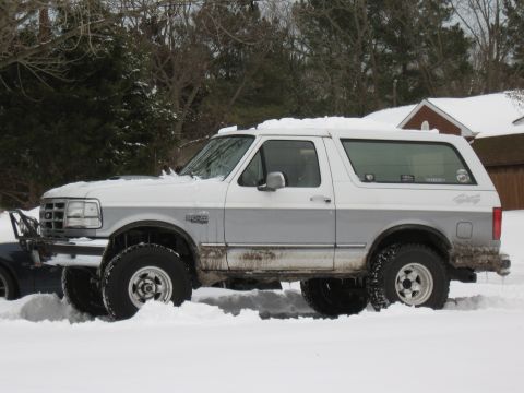 1994 Ford Bronco - This two-tone Ford Bronco is partially buried in snow, showing its side profile and lifted suspension.
