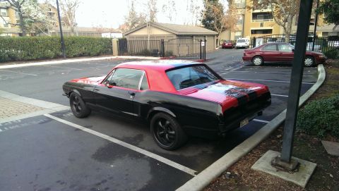 1987 Ford Bronco - Black 1967 Ford Mustang with a red roof and trunk stripe is parked in a lot.