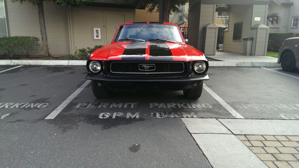 Red 1967 Ford Mustang with black racing stripes parked in a lot