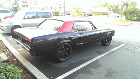 1987 Ford Bronco - A black classic coupe with a red roof and aftermarket wheels is parked in a lot next to a white SUV.