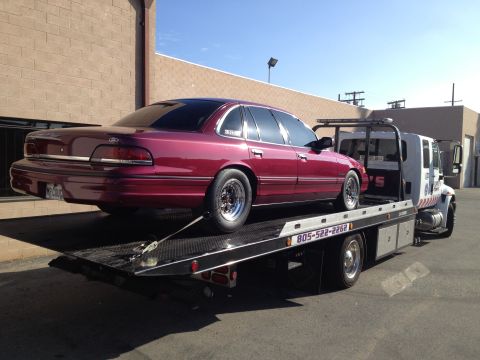 1992 Ford Crown Victoria - Maroon 1992 Ford Crown Victoria loaded onto a flatbed tow truck under a clear blue sky.