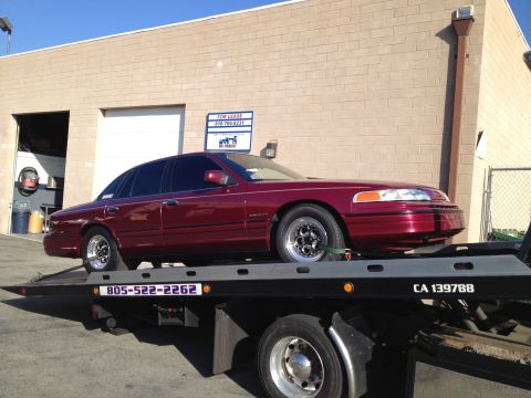 1992 Ford Crown Victoria - A maroon sedan, likely a Ford Crown Victoria from the late 1990s, is being transported on a tow truck.