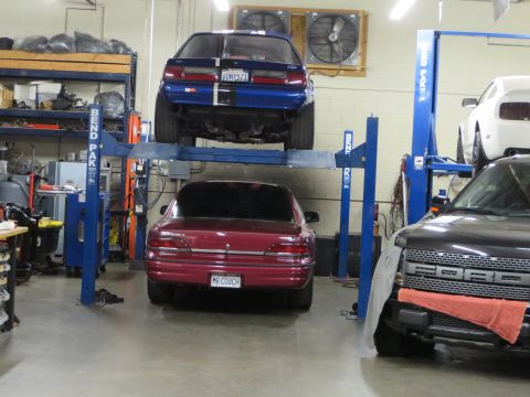 1992 Ford Crown Victoria - Two cars are on car lifts in a garage, with a third vehicle partially visible on the right.