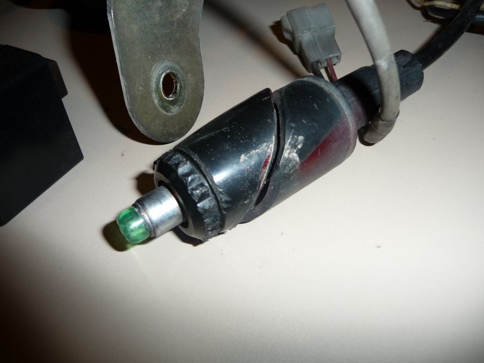 Black plastic automotive part with a green LED light and metal mounting bracket
