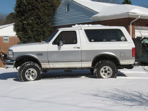 1994 Ford Bronco - A two-tone white and silver Ford Bronco sits partially buried in snow, its off-road tires.
