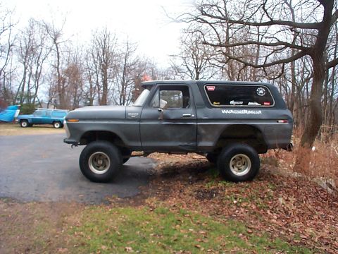 1979 Ford Bronco - Side view of a lifted gray Ford Bronco with stickers on the rear window and a blue station wagon behind it.
