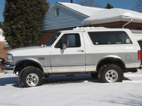 1994 Ford Bronco - White and silver Ford Bronco with a flat front tire sits in the snow.