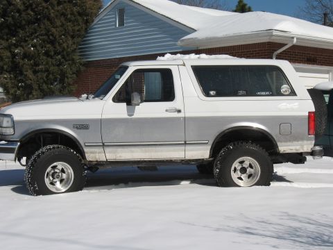 1994 Ford Bronco - A two-tone white and silver 1994 Ford Bronco sits parked in a snowy driveway.