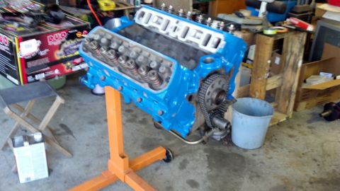 1988 Ford Bronco - A blue V8 engine block is mounted on an orange engine stand, with various garage items in the background.