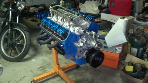 1988 Ford Bronco - A blue V8 engine is mounted on an orange stand, with a motorcycle visible in the background.