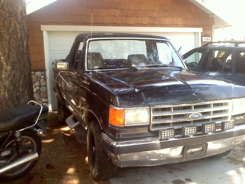 1988 Ford Bronco - This black Ford truck, likely a 1987 model, is parked in front of a garage with another vehicle visible.